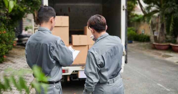 Two movers in gray uniforms inspecting and organizing cardboard boxes in the back of a truck, offering professional services as movers and packers NJ for efficient relocation.